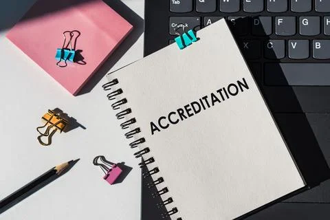 Notebook with tools and notes about ACCREDITATION lies on laptop. Stock Photos