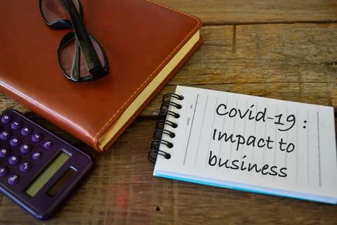 Notebook written with text COVID-19: IMPACT TO BUSINESS. Stock Photos