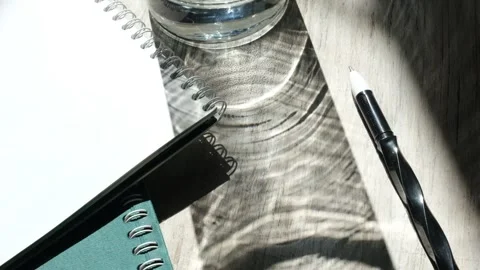 Notebooks, pen and hard shadow of glass vase. Workplace, Vidéo 160193552