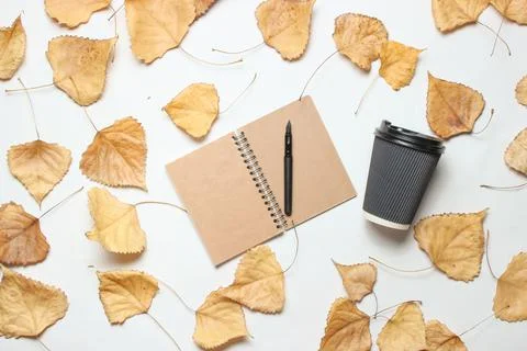 Notepad and cup of coffee on white background with fallen leaves. The concept Stockfoto's
