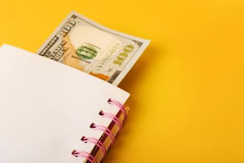 Notepad with banknote on yellow background. Dollar bill used as bookmark in b Stock Photos
