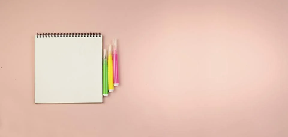 Notepad on a black spring and markers on a pink background. Stock Photos