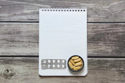 Notepad with a blank white sheet in a checker paper with pills in a blister l Stock Photos