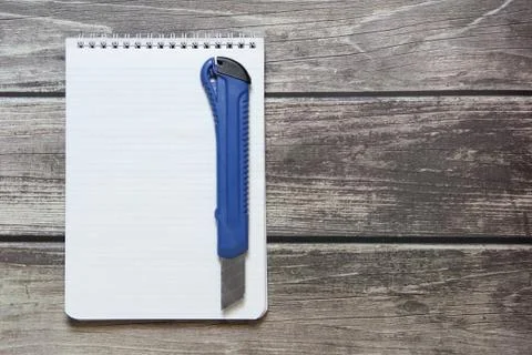 Notepad with a blank white sheet in a checker paper with stationery knife lie Stock Photos