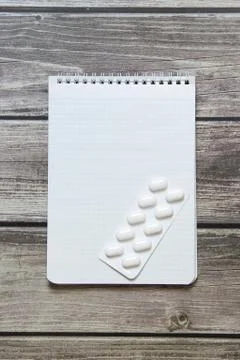 Notepad with a blank white sheet in a checker paper with pills in a blister l Stock Photos