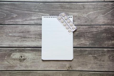 Notepad with a blank white sheet in a checker paper with pills in a blister l Stock Photos