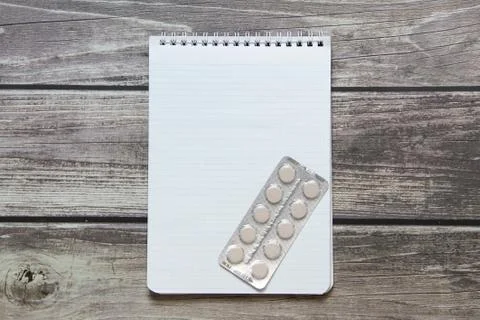 Notepad with a blank white sheet in a checker paper with pills in a blister l Stock Photos