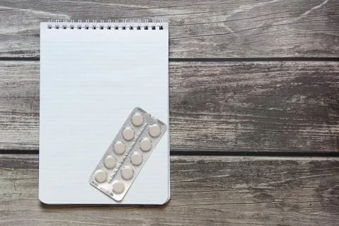 Notepad with a blank white sheet in a checker paper with pills in a blister l Stock Photos