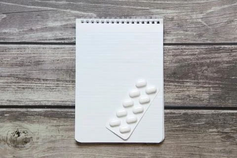 Notepad with a blank white sheet in a checker paper with pills in a blister l Stock Photos