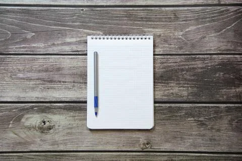Notepad with a blank white sheet in a checker paper with ball pen lies on the Stock Photos