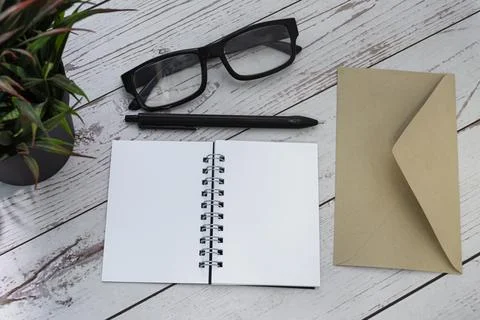 Notepad with brown envelop, reading glasses, pen and potted plant on wooden desk Stock Photos