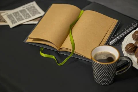 Notepad, chocolates, a cup of coffee and old flyers on a black background. Stock Photos