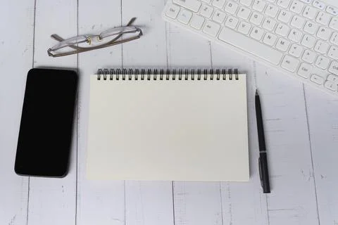 Notepad with computer keyboard, smartphone, pen and reading glasses on a desk Stock Photos