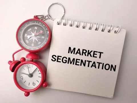 A notepad displaying MARKET SEGMENTATION rests beside a red alarm clock com.. Stock Photos