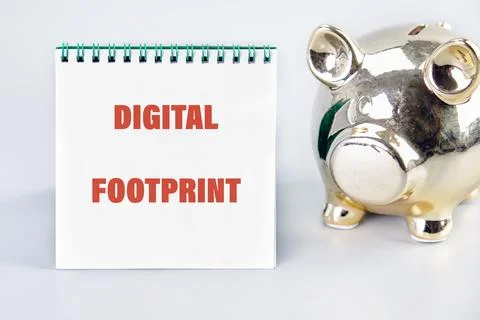 A notepad displaying the term digital footprint sits next to a shiny piggy ba Photos