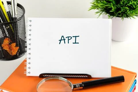 Notepad displaying the word API is set on a desk surrounded by a magnifying g Stock Photos