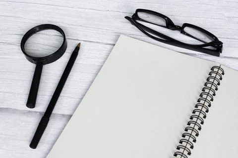 Notepad flat lay with magnifying glass and pen on white wooden desk. Copy spa Stock Photos