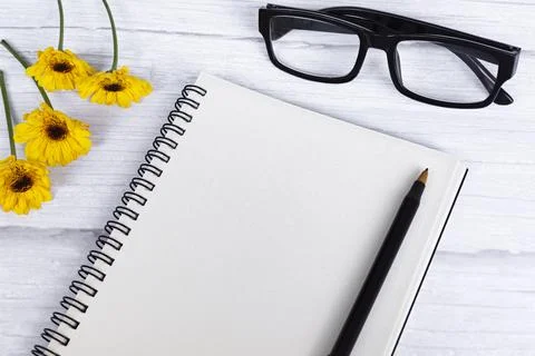 Notepad flat lay with sunflowers, reading glasses and pen on wooden desk. Stock Photos