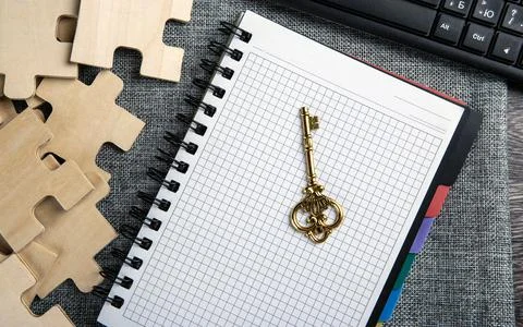 Notepad with a gold key symbol, pc keyboard and puzzle pieces Stock Photos