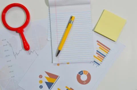 Notepad, graph, pens and lens on a table Stock Photos