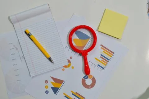 Notepad, graph, pens and lens on a table indicating a work area Stock Photos