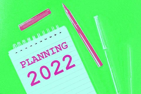 Notepad labeled Planning 2022  and multi-colored markers on light green Stock Illustration