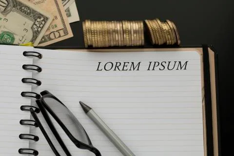 Notepad with Lorem ipsum words, pencil, glasses and dollar banknotes Stock Photos