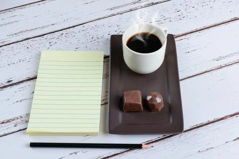 Notepad next to a cup of coffee and dark chocolate candies. Stock Photos