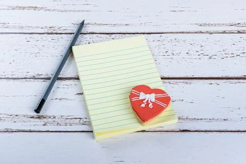 Notepad next to a graphite pencil and a heart-shaped cookie. Stock Photos