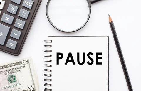Notepad with pause written on it, sitting next to a calculator and pen on a d Foto stock