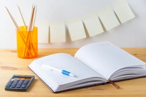 Notepad with pen container with pencils, calculator are on a wooden table. .. Stock Photos