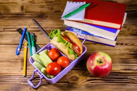 Notepad, pens, ripe apple, stack of books and lunch box with hamburger, cucum 스톡 사진