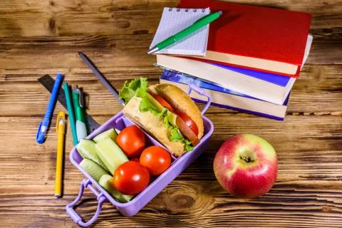 Notepad, pens, ripe apple, stack of books and lunch box with hamburger Stock Photos