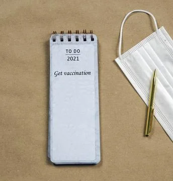 Notepad with protective face mask and gold pen, New Year goal get vaccination Stock Photos