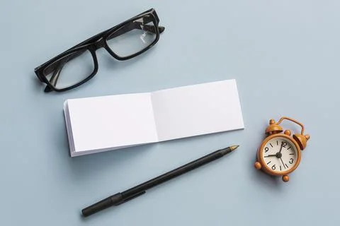 Notepad with reading glasses, pen and alarm clock on blue background Stock Photos