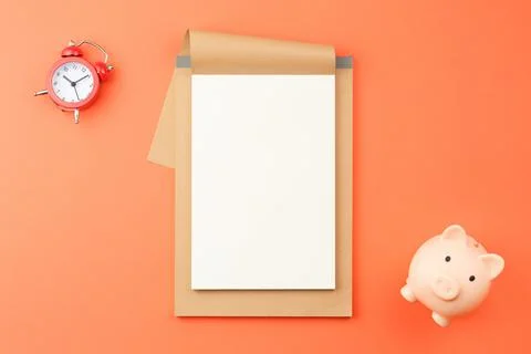 Notepad with red alarm clock and pig piggy bank. Stock Photos