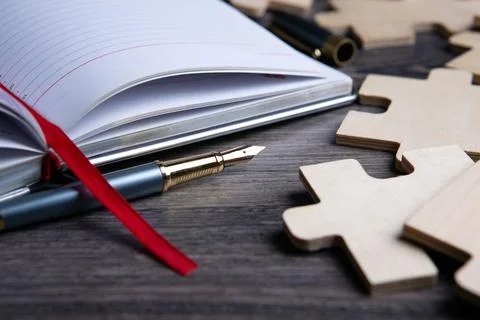 Notepad with ribbon bookmark and a fountain pen and puzzle pieces Stock Photos