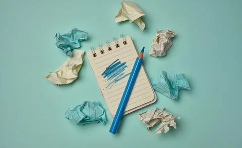 Notepad with a scribbled page and blue pencil surrounded by crumpled paper .. Fotos de archivo