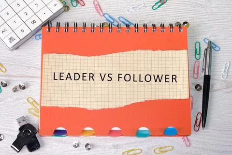 A notepad shows the words leader vs follower. Nearby are a pen, paper clips,  Фото