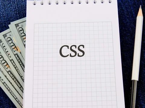A notepad with the term CSS written in grid format next to bundles of banknot 스톡 사진