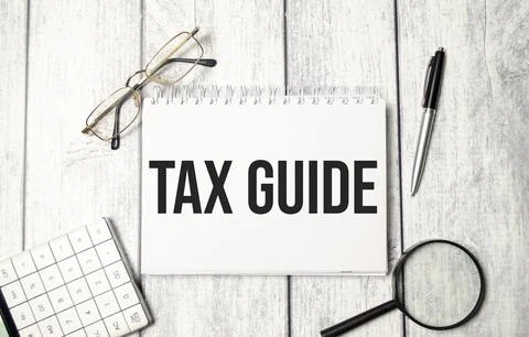 A notepad with the text TAX GUIDE, a pen, calculator and glasses Fotos de archivo