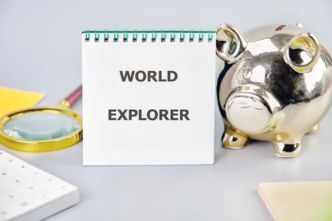 Notepad titled World Explorer sits next to a shiny piggy bank and a magnifyin Stock Photos