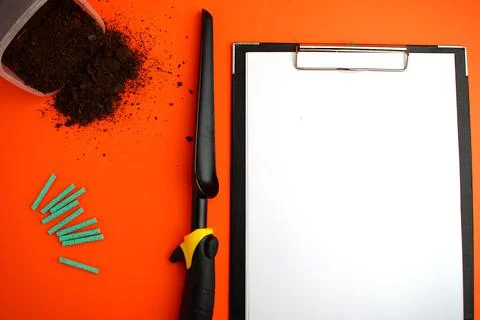Notepad with a white sheet of paper, next to the ground, garden shovel and gr Stock Photos