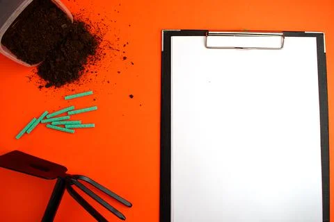 Notepad with a white sheet of paper, next to the ground, garden hoe and green Stock Photos