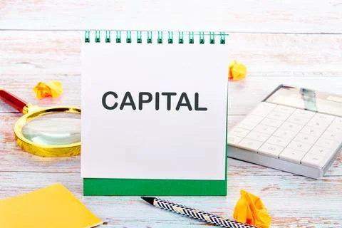 A notepad with the word capital written in large letters sits on a wooden d.. 스톡 사진