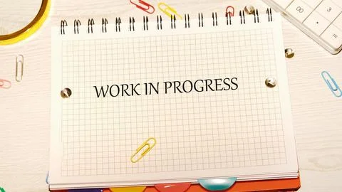A notepad with Work in Progress written on it rests on a textured wood surface Stock Photos