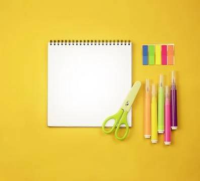 Notepad on a yellow background, colored markers and green scissors. Stock Photos