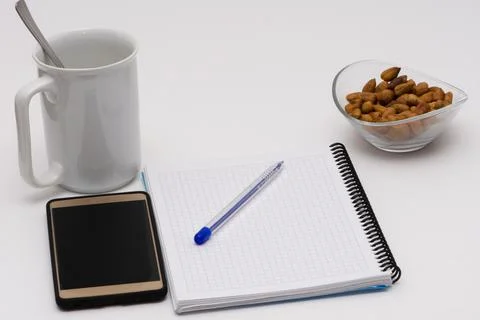 Notes, pen, smart phone, empty cup and the glass bowl filled with hazelnuts Stock Photos