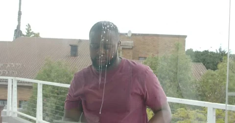Noticing soap drips, man in maroon T-shirt squeegeeing balcony glass with cloth, Stock Footage 336844871