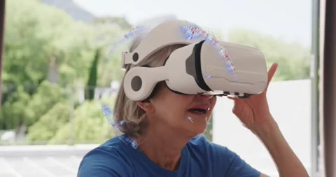 Noticing VR headset resting on table, elderly woman lifting device and exploring Stock Footage 320415896